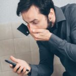 Homem surpreso olhando o celular e segurando um cartão
