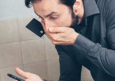 Homem surpreso olhando o celular e segurando um cartão